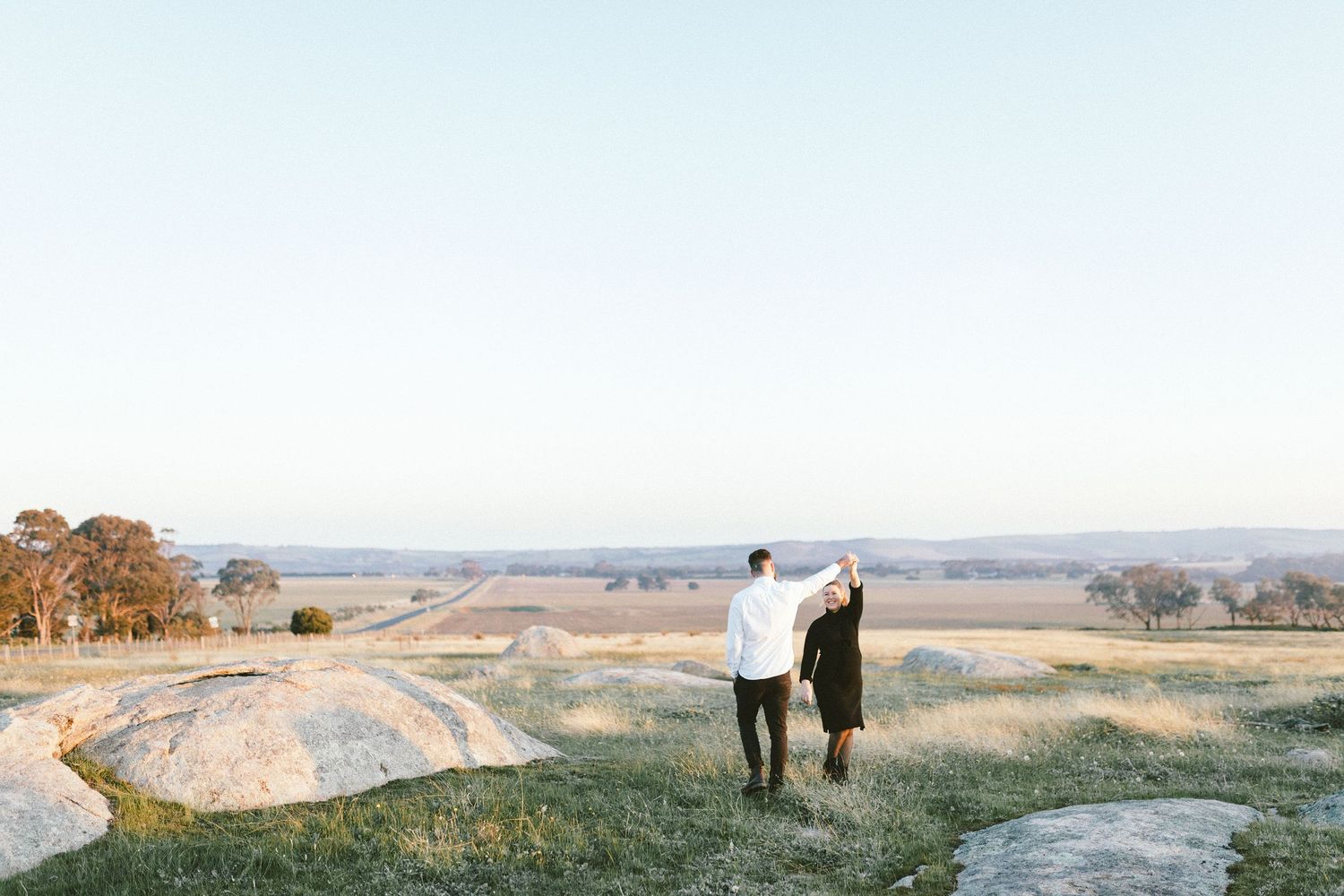 Two figures explore a scenic hilltop path with panoramic valley views in the distance.