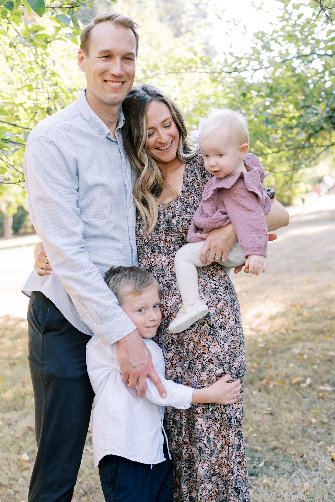 A sunny outdoor family portrait with natural lighting and greenery in the background.