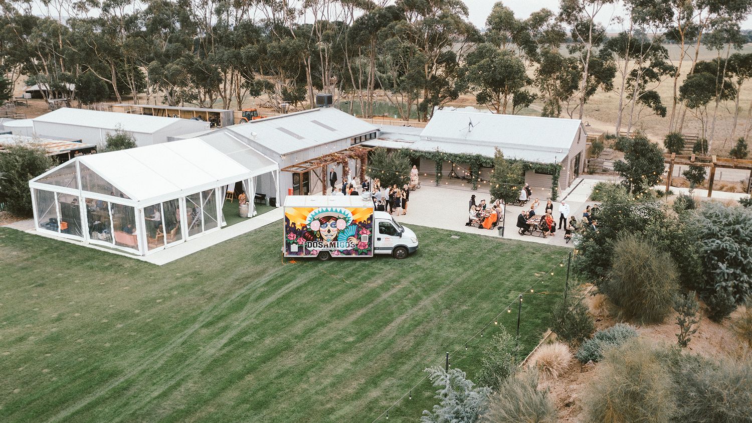 Aerial view of white wedding tent and food truck setup on green lawn.