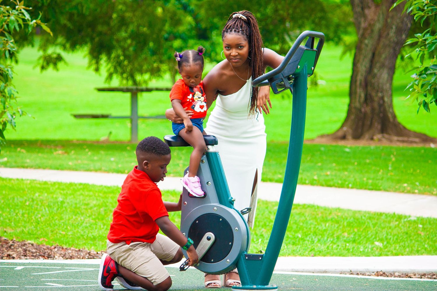 Family enjoying outdoor exercise equipment together in a lush green park setting.