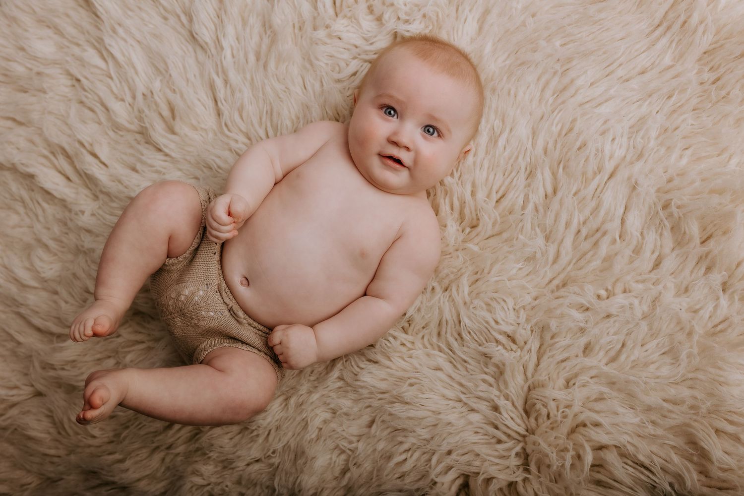 Baby lounges on plush white fur rug during professional portrait session.