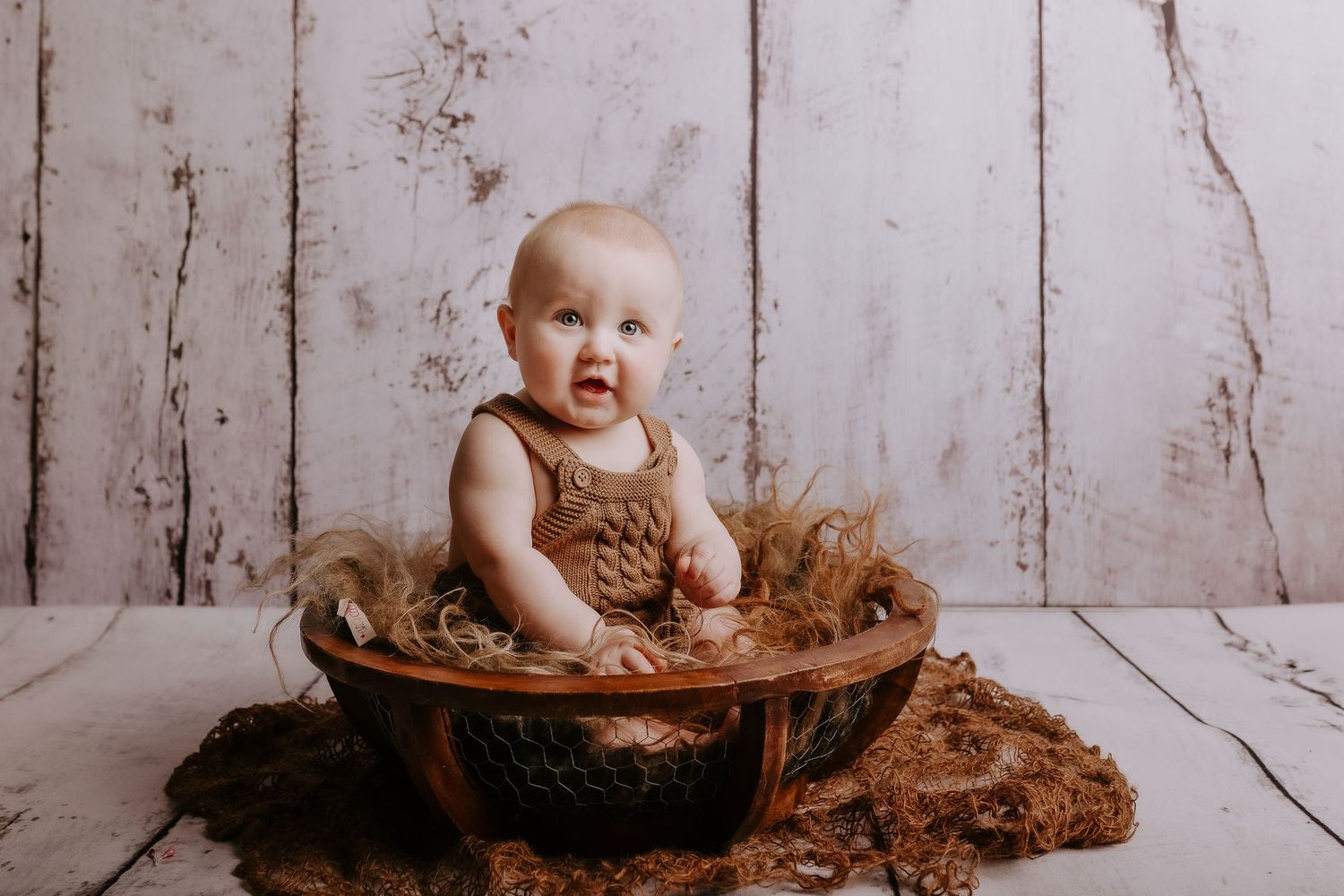 Baby sitting with teddy bear on rustic white wooden background during portrait session.