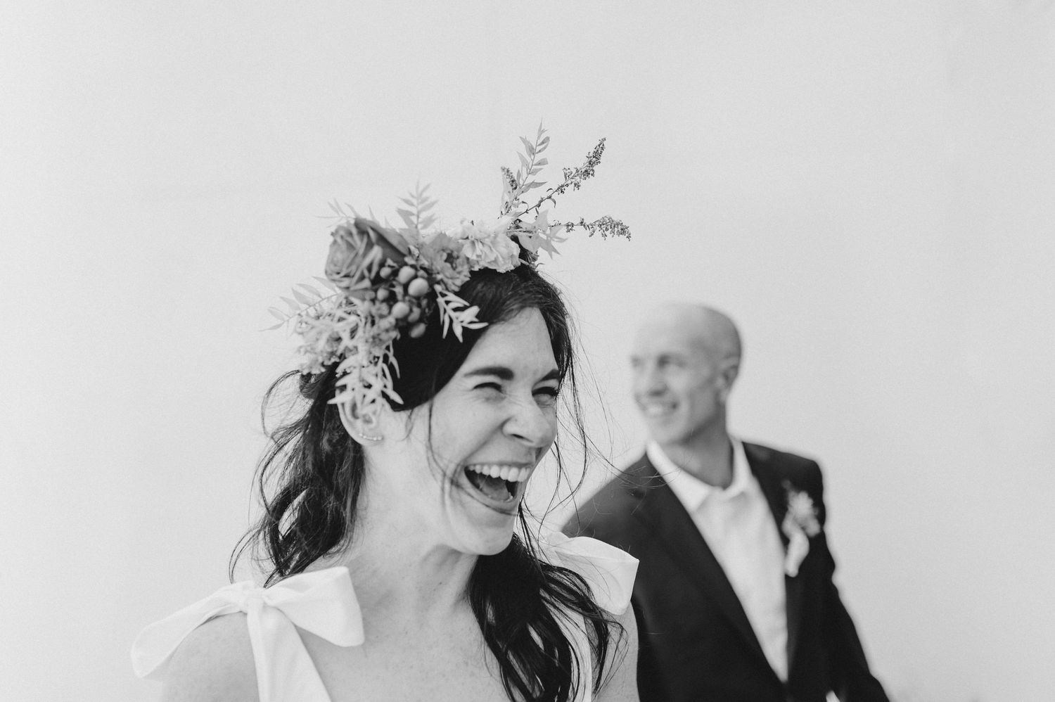 A black and white candid wedding moment showing laughter and joy with floral crown details.
