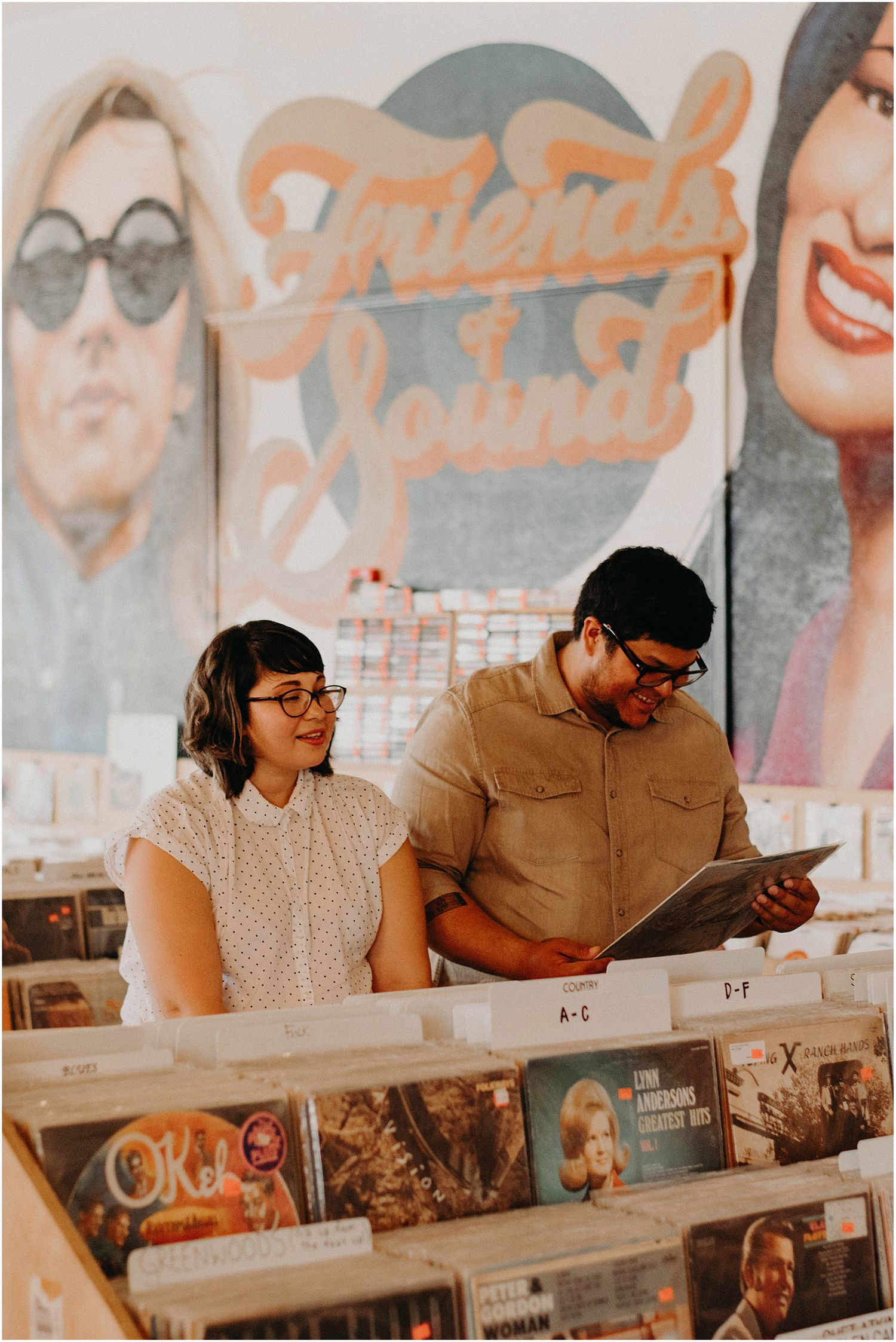 A couple browses through vinyl records together at a retro music store with vintage posters on the wall.