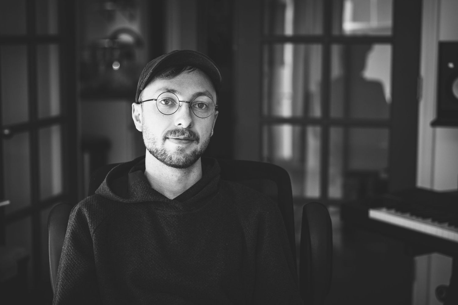 photographer wearing a black hat and round glasses sitting in an office studio