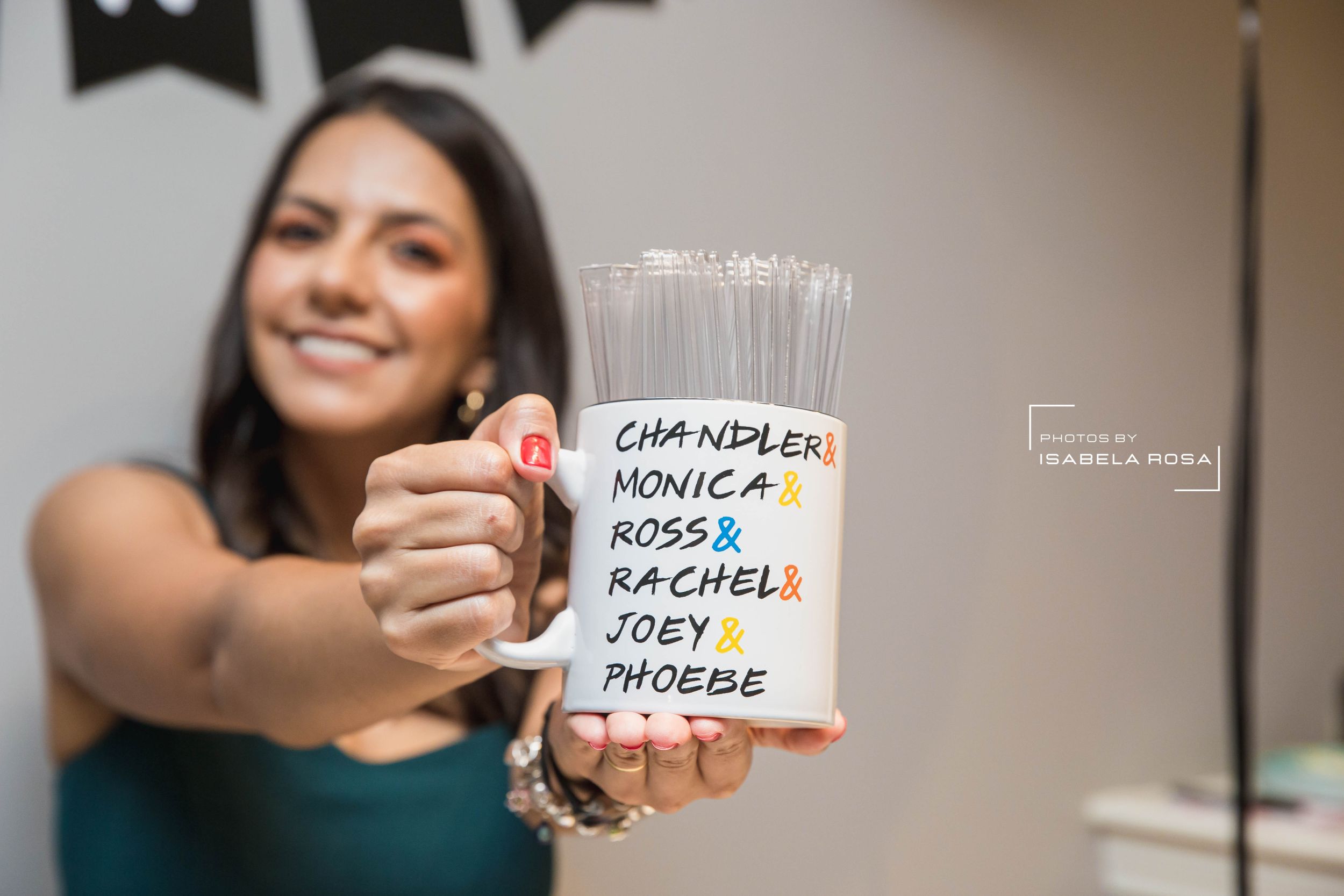 Hand holding a white mug with Friends TV show character names written on it.