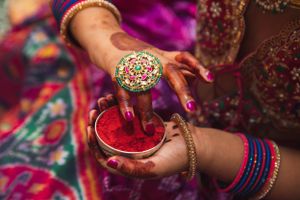 Hands adorned with traditional Indian jewelry and bangles holding kumkum powder during a cultural ceremony.