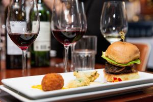 Elegant food and wine pairing with burger, croquette and red wine glasses.