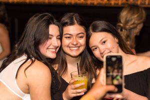 Friends taking selfies and enjoying drinks at a dimly lit bar.
