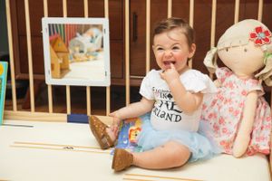 Happy toddler sitting with stuffed toys and books in a nursery setting.