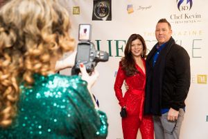 Photographer taking photo of couple posing at formal event with logo backdrop.