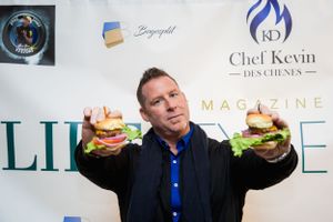 Man in blue shirt holding up two large hamburgers at promotional event.