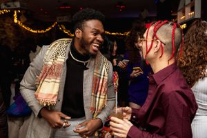 Friends laughing and socializing at a festive party with string lights in background.