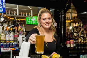 Bartender serving a golden beer at busy bar with liquor bottles in background.