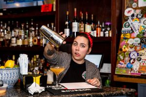 Bartender pouring a cocktail into a decorated glass at a fully stocked bar.
