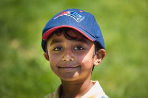 Young person wearing a New England Patriots baseball cap smiles outdoors on sunny day.
