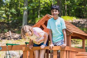 Children playing together on wooden playground equipment in wooded area.