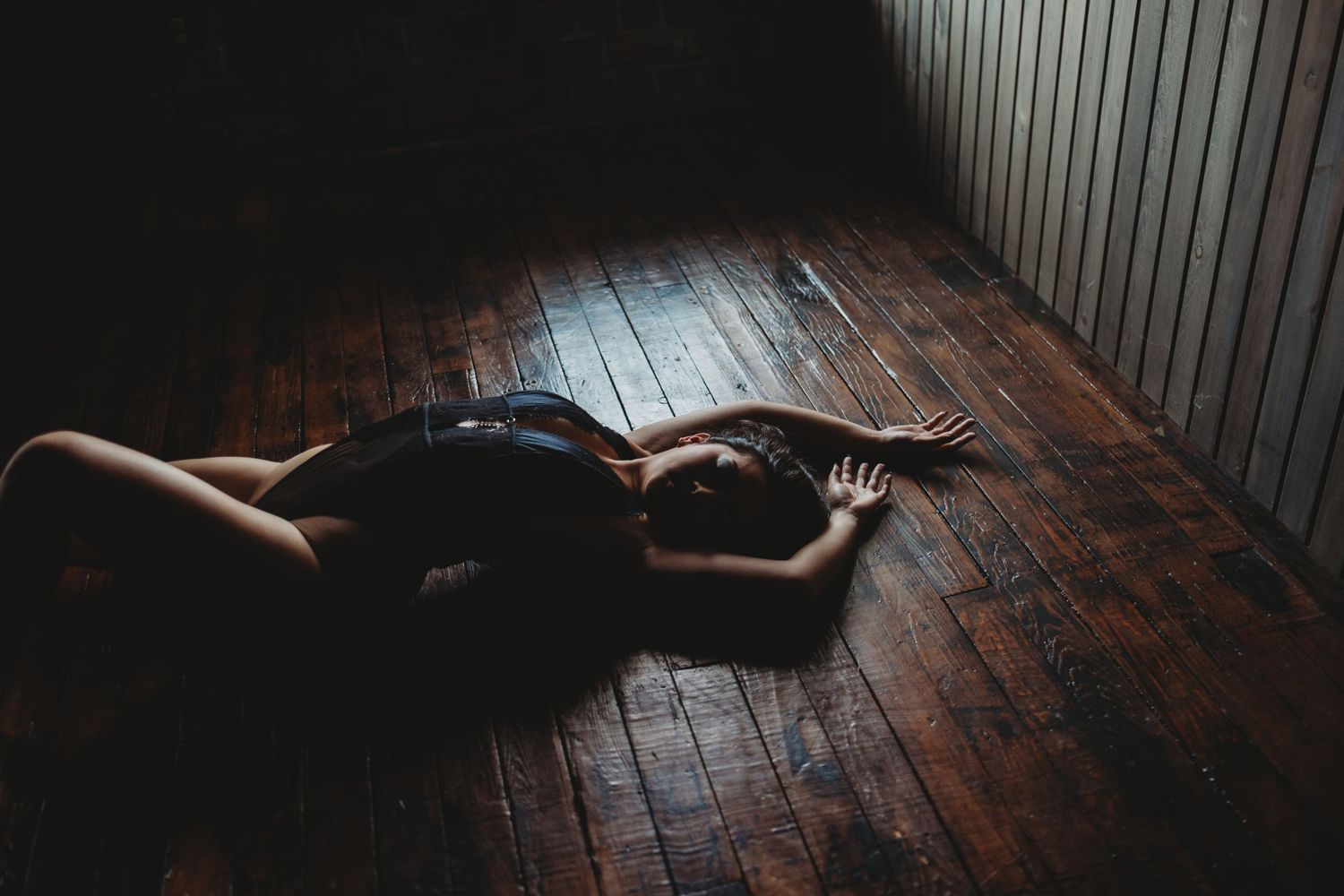 Dramatic low-key photography on dark wooden floorboards with natural window lighting.