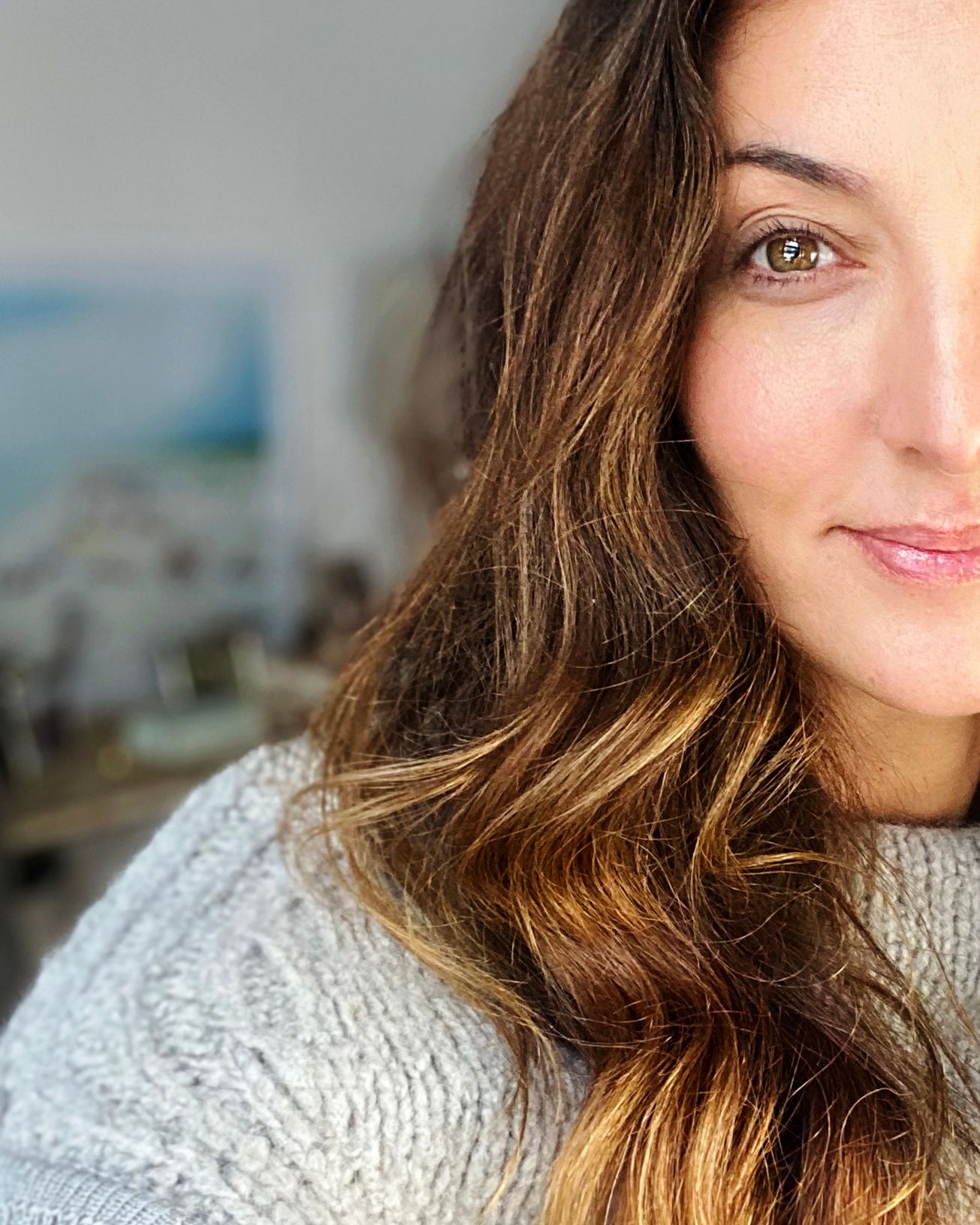 Close-up portrait of a Cristina Coco with wavy brown highlighted hair wearing a cozy gray knit sweater.