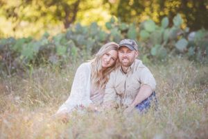 Couple sits together in golden sunlit field with cactus plants in background.