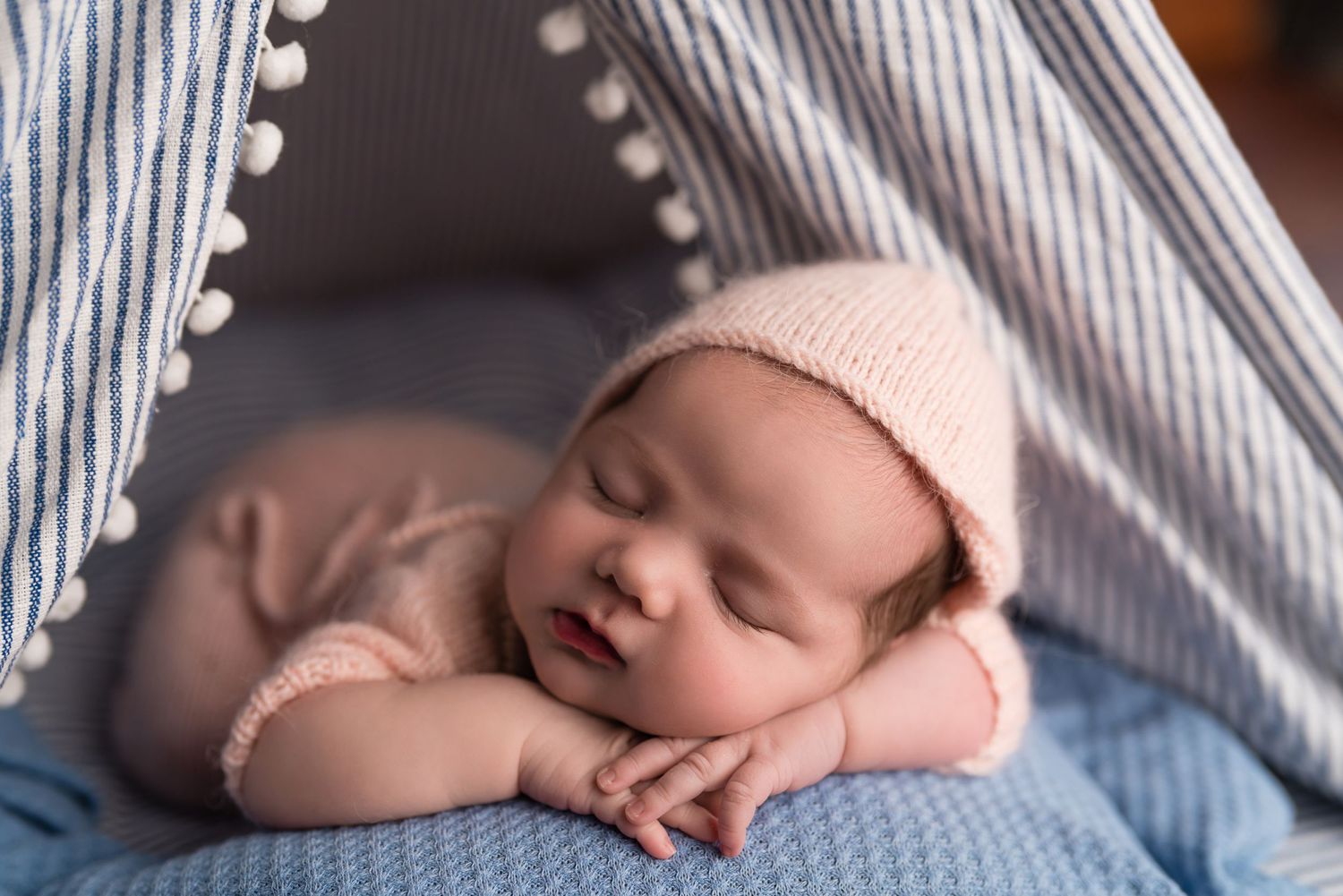Sleeping newborn in pink hat resting on striped blue and white fabric.