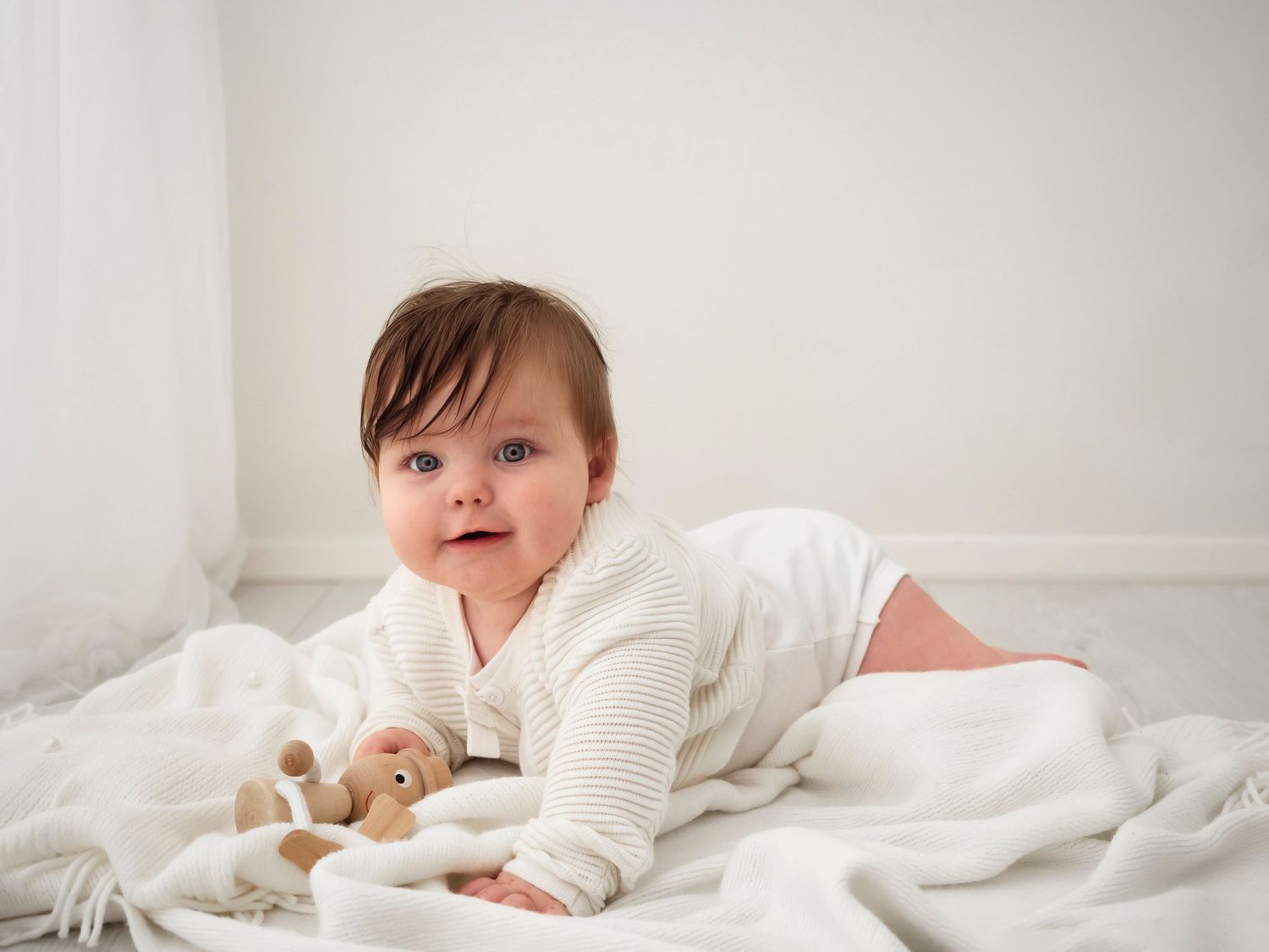 baby girl in white smiles at camera during a photoshoot