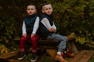Two children in coordinating outfits sitting side by side on a wooden bench outdoors.