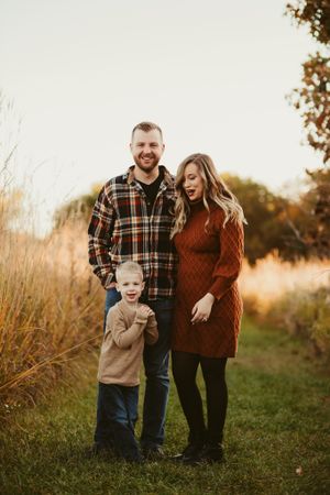 A candid family portrait taken at golden hour with tall grass and trees in the background.