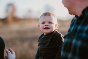 Close-up portrait of a smiling toddler in a black sweater during sunset.