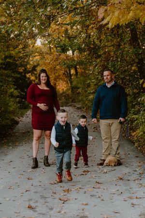 Family walking together on a leaf-covered path during fall with beautiful golden foliage overhead.