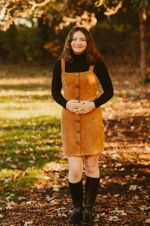 Person wearing corduroy dress and black turtleneck poses in autumn forest setting.