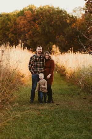 A family poses together on a grassy path with tall golden grasses and autumn trees at sunset.