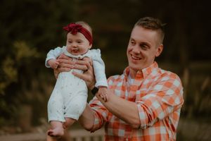 A tender moment between parent and baby in matching orange plaid and white outfits during an outdoor photo session.