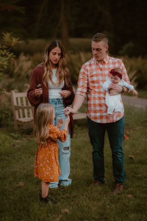 Family of four spending time together outdoors with baby and toddler in autumn setting.