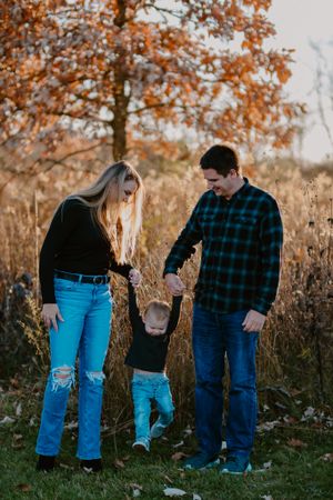 Family playing together outdoors among tall grass and autumn foliage at sunset.