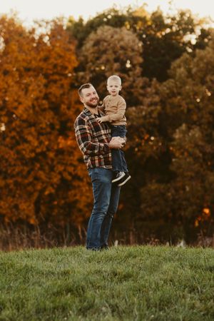 Father and child standing in field with autumn trees in background.