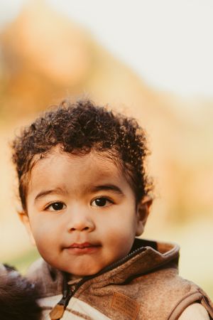 Close up portrait of toddler in brown vest against autumn background.
