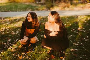 Two people sitting on grass during golden hour in autumn setting.