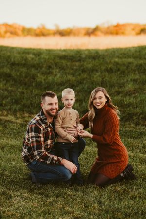 Family portrait on grassy hill with warm sunset lighting in background.