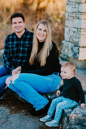 Family of three sitting together on stone steps during golden hour in casual attire.