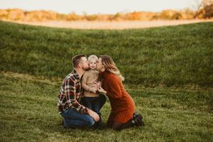 Intimate family moment captured on grassy hillside during golden hour.