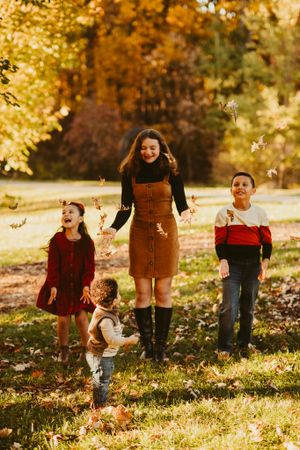 Children and adult playing among falling autumn leaves in a park setting.