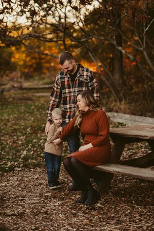 Family sits together on a wooden bench surrounded by fall foliage and leaves.