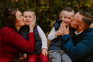 Sweet family moment with parents kissing their children's cheeks on a wooden bench.