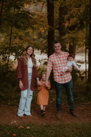 A fall family portrait set against trees with warm autumn colors.