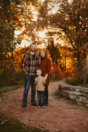 Family portrait on dirt path with stone wall and golden sunset through autumn trees.