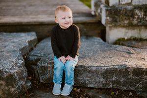 Young child in black sweater and jeans sitting alone on concrete steps outdoors.
