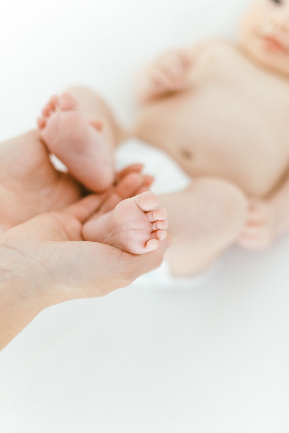 Close-up of tiny baby feet being held by adult hands against white background.