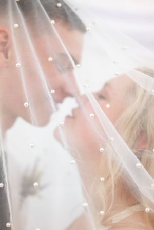 Dreamy wedding portrait through pearl-dotted veil as couple shares intimate moment.