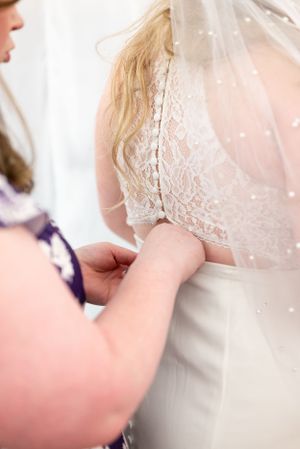 Detail shot of hands adjusting delicate lace on back of wedding gown.